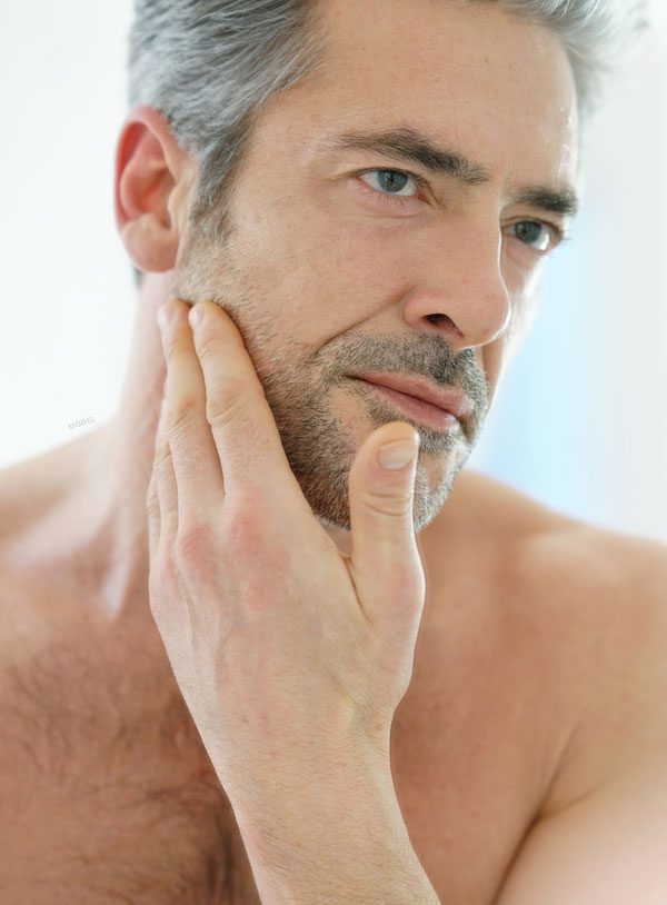 Middle aged shirtless male model rubbing her bearded face and looking in an unshown mirror